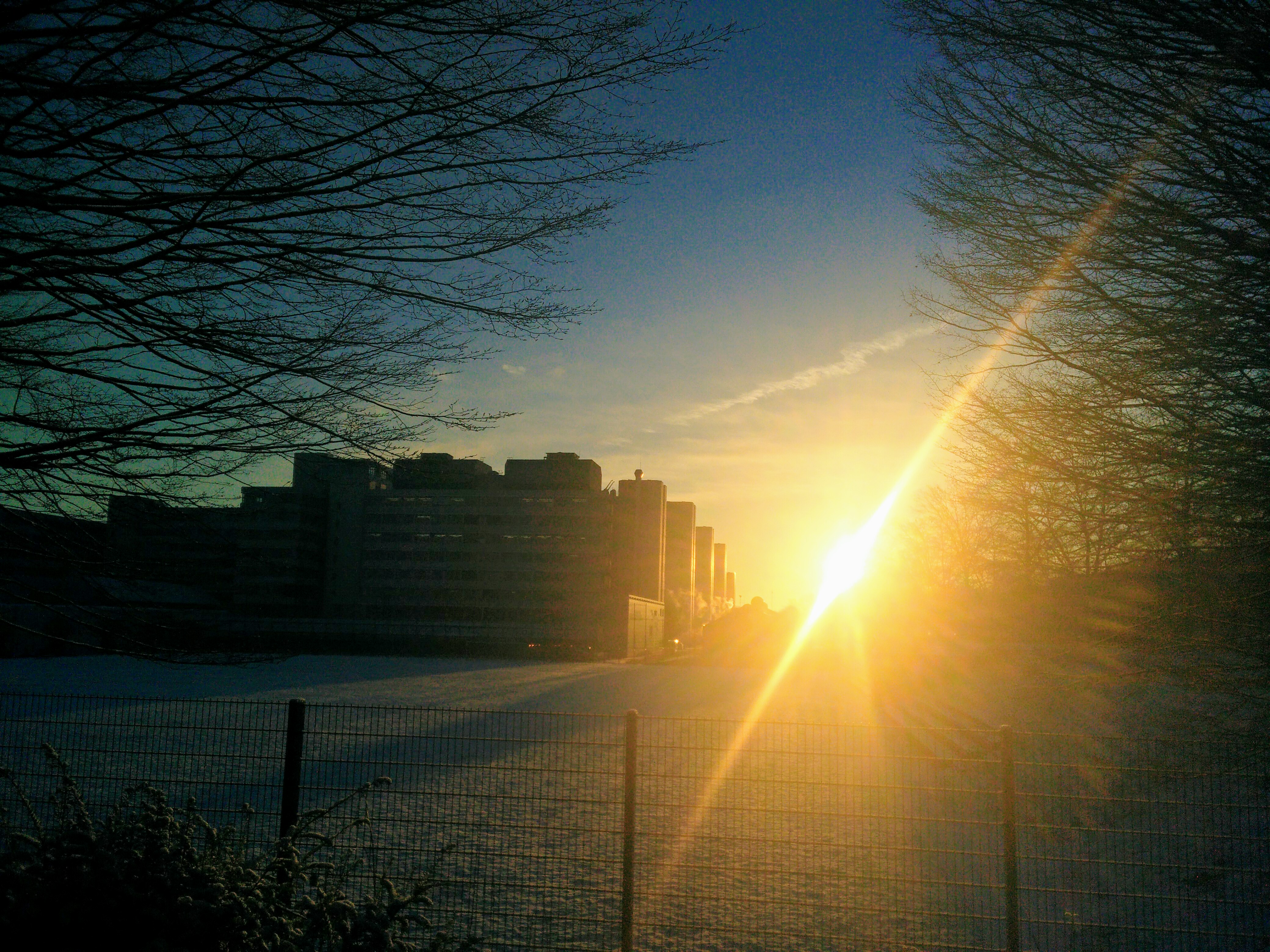 Die Universität Bielefeld im Gegenlicht. Man sieht die Umrisse des Gebäudes und helle Sonnenstrahlen.